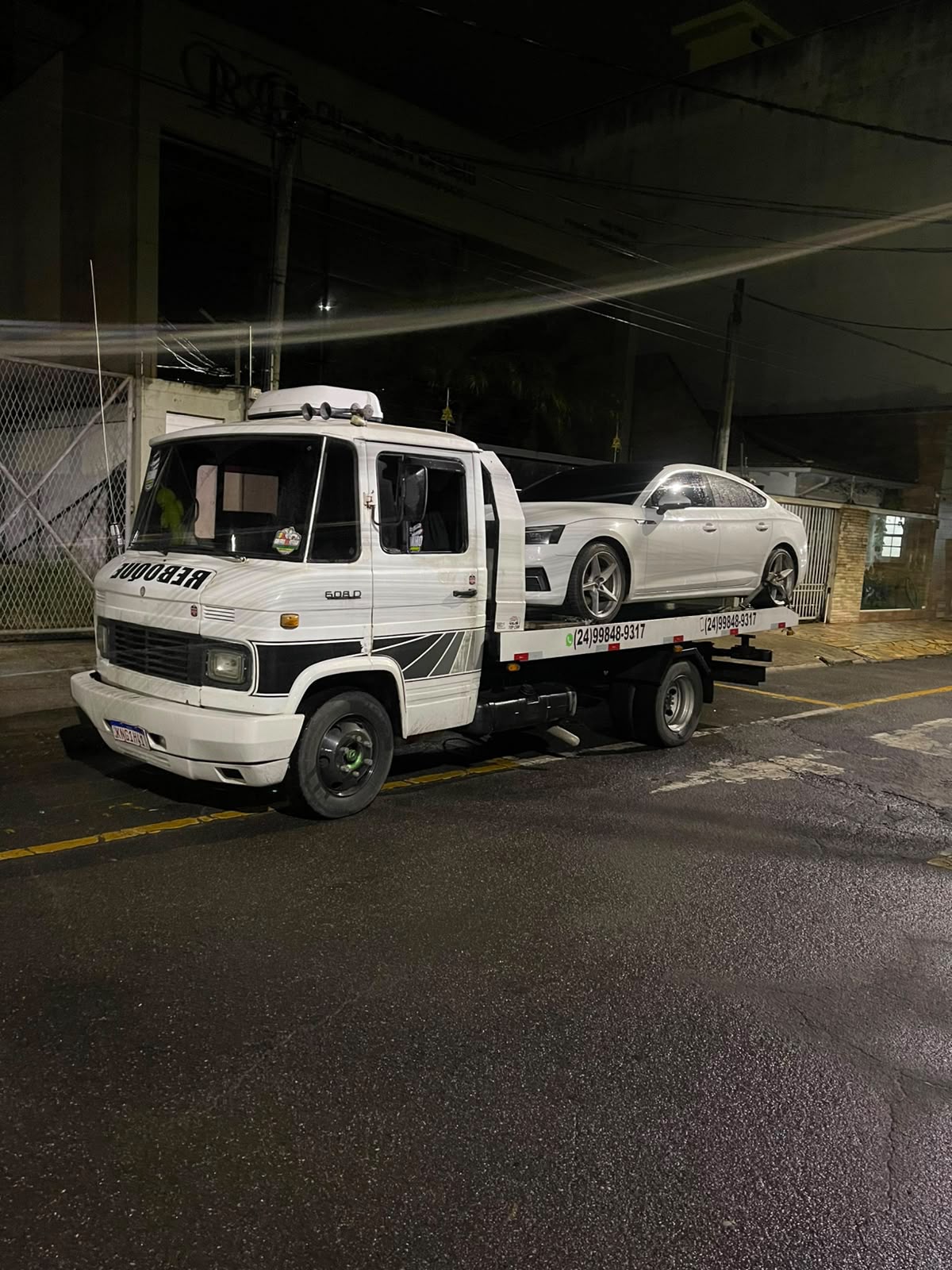 Guincho transportando carro branco à noite com telefone visível