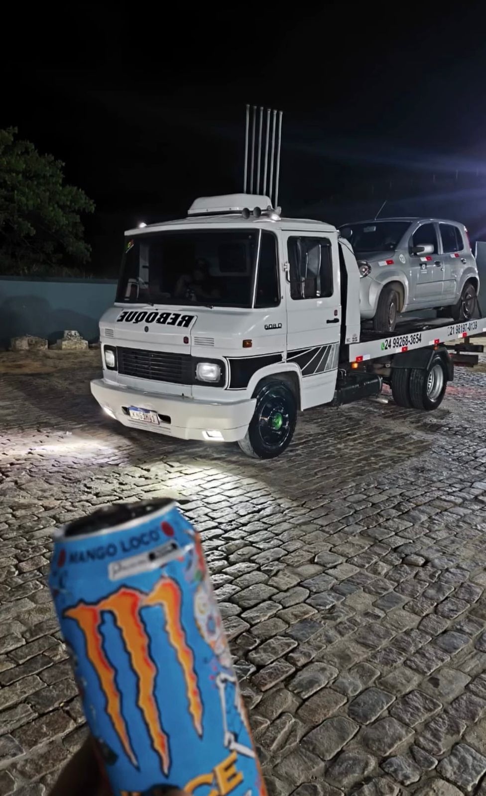 Caminhão-guincho realizando reboque em rua de pedra à noite