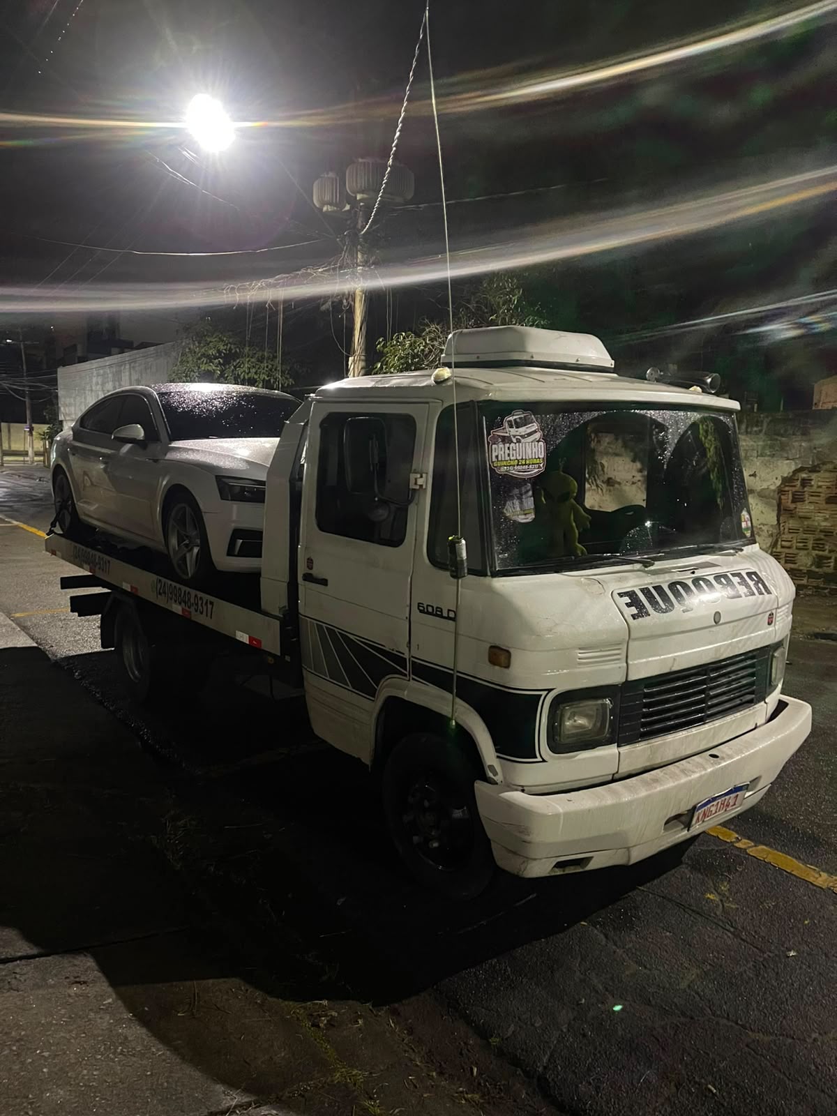 Caminhão-guincho transportando carro à noite com logo visível