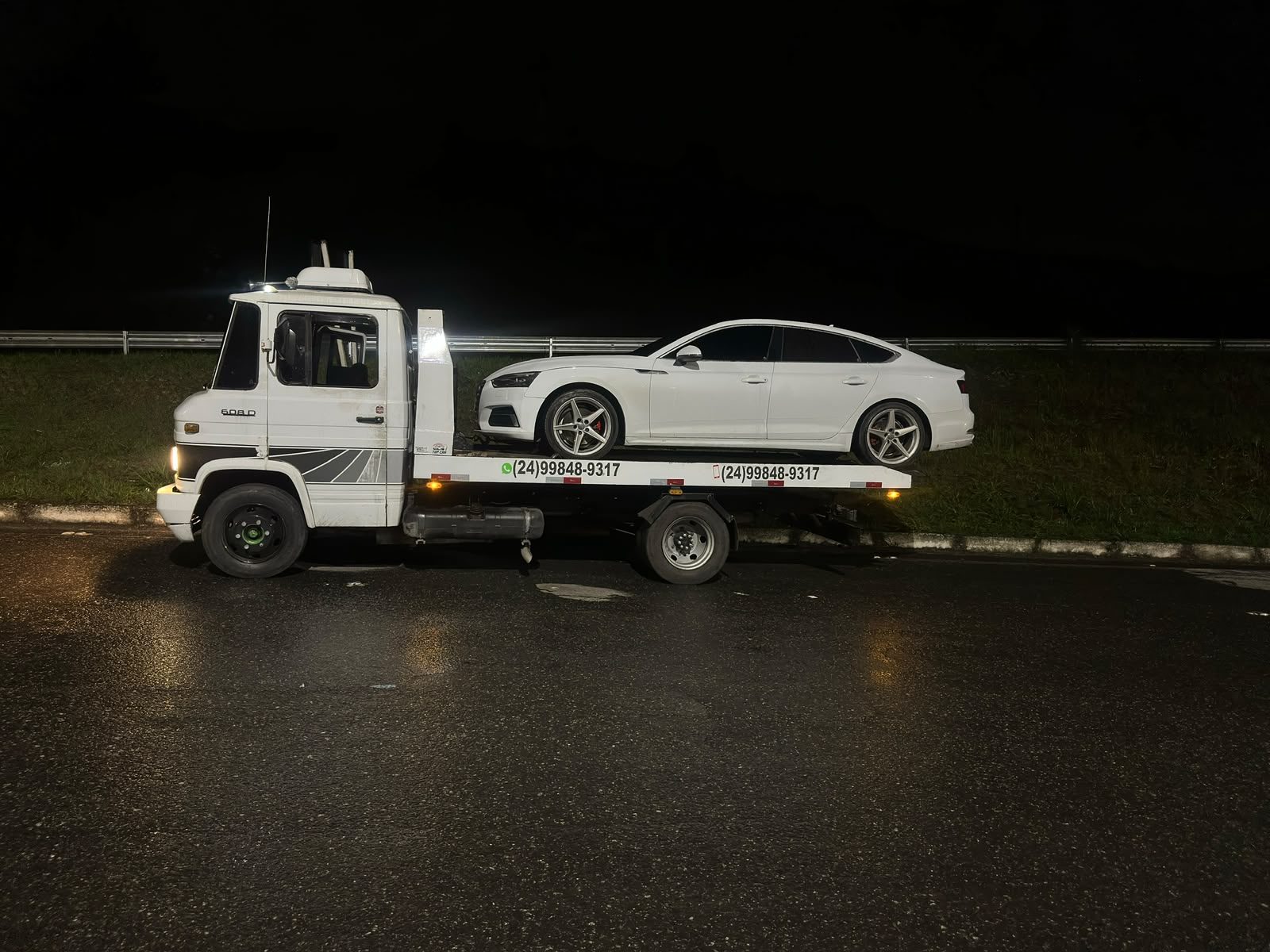 Guincho plataforma rebocando sedan branco à noite